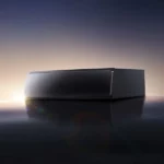 Hesai ATX compact automotive LiDAR sensor with 140° x 20° field of view photographed against sunset horizon, showing sleek black housing with reflective surface and lens flare effect